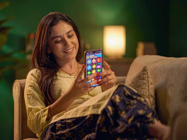 lucky777 Woman relaxes on a sofa and smiles at a phone showing a colourful slot game