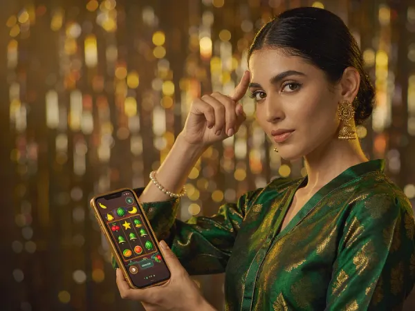lucky777 Woman in an emerald and gold kameez holds a phone showing glowing fruit and bell reels