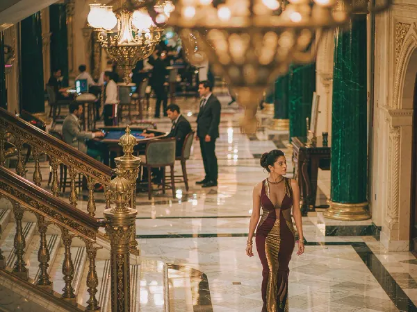 lucky777 Woman in a maroon and gold dress walks through a chandelier-lit casino lobby